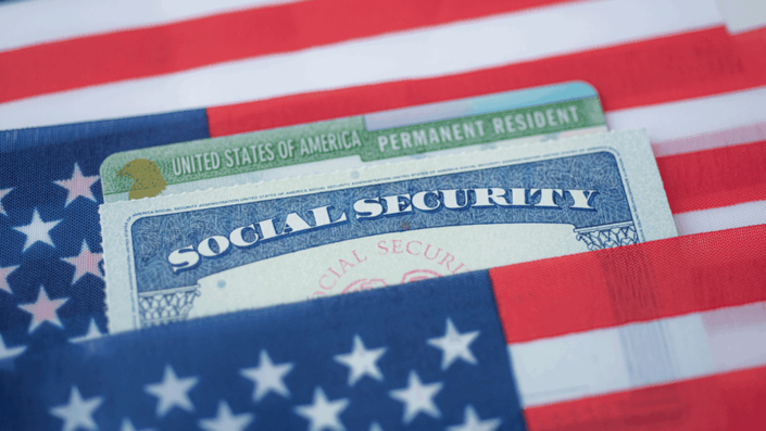 Tarjeta de Seguro Social de EE. UU. y tarjeta de Residente Permanente (Green Card) parcialmente visibles, metidas en un pliegue de la bandera estadounidense, ilustrando la documentación relacionada con la apertura de una cuenta bancaria sin SSN.