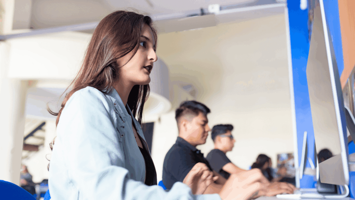 Jóvenes estudiantes concentrados trabajando en computadoras en un aula moderna, simbolizando el esfuerzo académico y la vida universitaria.
