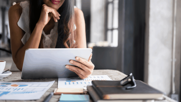 Mujer usando una tablet, revisando documentos financieros y gráficos en un ambiente de oficina, representando la gestión y análisis de fondos comunes de inversión.