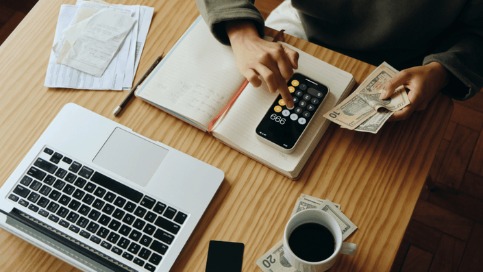 Persona calculando con una calculadora y contando dinero, reflejando la gestión financiera personal relacionada con el historial crediticio.