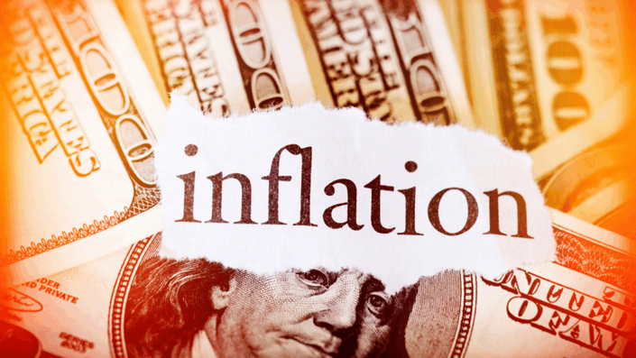 Papel rasgado con la palabra "inflation" (inflación) superpuesto sobre billetes de cien dólares estadounidenses, con un tinte anaranjado cálido, representando el concepto de inflación y su impacto en el dinero.