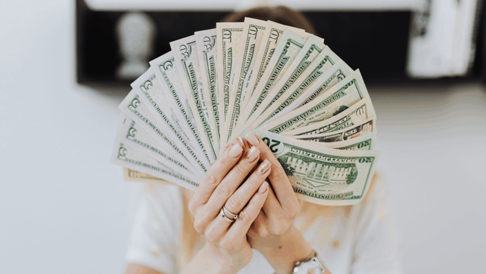Persona sosteniendo una cantidad de billetes de dólar, representando la posibilidad de aumentar ingresos extra mediante diversas estrategias financieras.