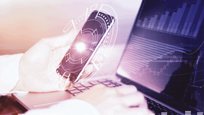 Persona usando una laptop y sosteniendo un smartphone con una interfaz gráfica futurista superpuesta, simbolizando la innovación tecnológica en las fintechs y el análisis de datos financieros.