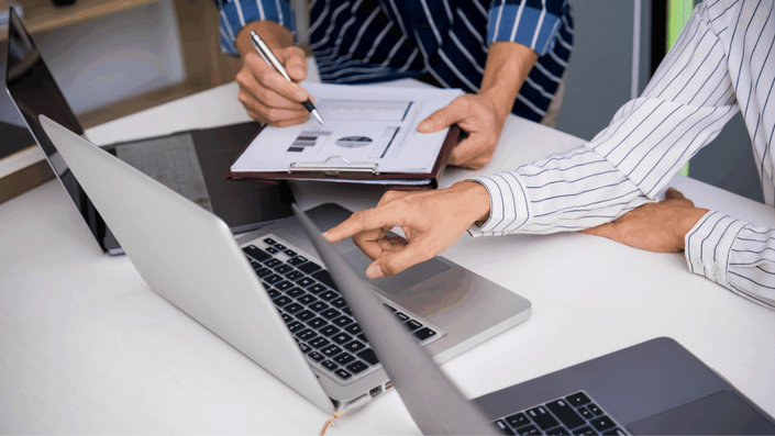 Equipo de trabajo discutiendo estrategias de inversión frente a laptops y gráficos financieros para maximizar rendimientos.