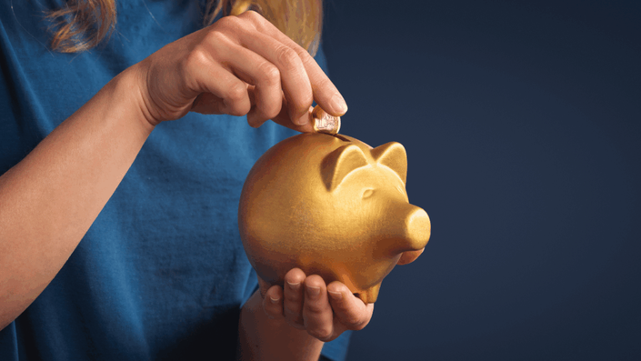 Mano depositando una moneda en un cofre dorado, representando el hábito del ahorro y la importancia de la inversión para el crecimiento financiero.