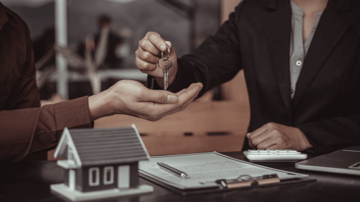 Persona entregando llave a otra sobre mesa con calculadora y contrato, ilustrando la transferencia y cierre de operaciones en inversiones inmobiliarias.
