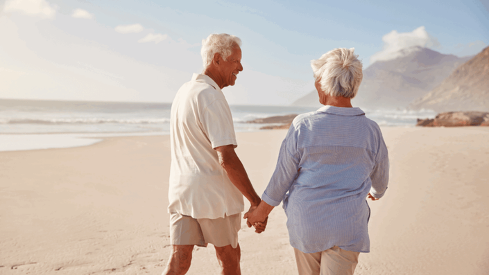 Pareja de adultos mayores caminando de la mano por la playa, disfrutando de su tiempo juntos gracias a un buen Ahorro para la jubilación.
