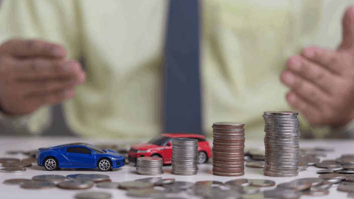 Manos de una persona detrás de varias pilas de monedas de alturas decrecientes junto a dos coches de juguete, simbolizando la pérdida de poder adquisitivo y el impacto de la inflación.