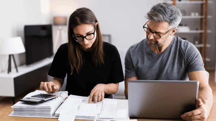 Pareja revisando facturas y usando una calculadora y una laptop para administrar su presupuesto familiar en una mesa de madera.