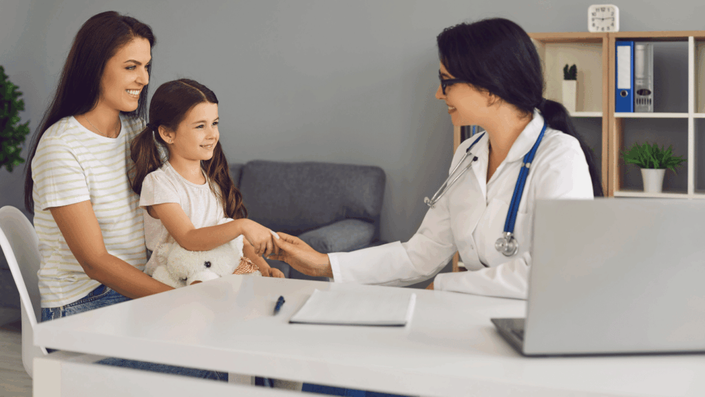 Madre e hija sonrientes en consulta médica con una doctora, simbolizando acceso a seguro médico económico y atención de calidad para la familia.