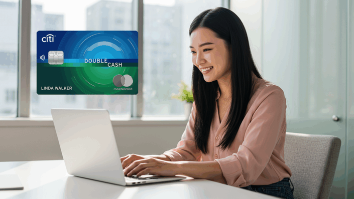 Mujer joven sonriendo mientras trabaja en su computadora portátil en una oficina iluminada, con una imagen destacada de la tarjeta Citi Double Cash Mastercard flotando a su lado.