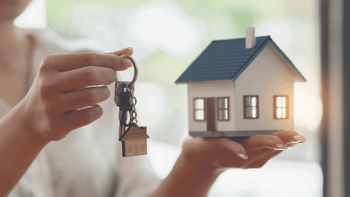 Manos sosteniendo llaves y una casa modelo, simbolizando la inversión en bienes raíces y la consideración de los REITs como una tendencia de inversión.